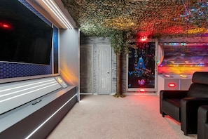 A room with a large flat-screen TV, a massage chair, a door, and a wall with a decorative light installation. - 8BR Windsor Westside Home w/ Private Pool (Kissimmee)