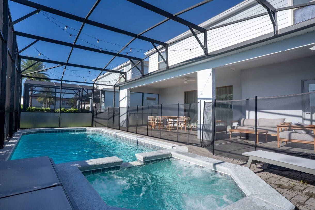 A pool area with a glass-enclosed patio, outdoor seating, and a hot tub.