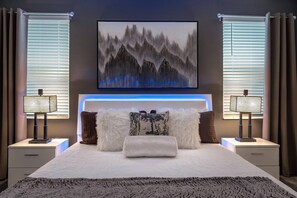 A modern bedroom with a large bed, a headboard with integrated lighting, two bedside tables with lamps, and a painting above the bed. - Bookmark Villa 8BR @ Storey Lake w/ Pool (Kissimmee)