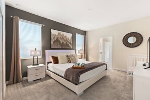 Ein Schlafzimmer mit einem großen Bett, Nachttischen, einem Babybett und einem wandmontierten Spiegel.