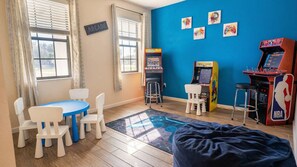 A room with arcade games, a blue wall, a table with chairs, and a bean bag. - 6BR Home w/ Private Pool Near Disney (Kissimmee)