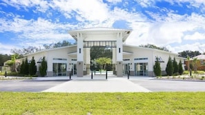 A modern building with a central entrance, surrounded by greenery and a clear sky. - 6BR Home w/ Private Pool Near Disney (Kissimmee)