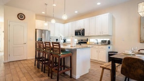 A modern kitchen with white cabinets, stainless steel appliances, and a central island with bar stools. - 6BR Home w/ Private Pool Near Disney (Kissimmee)