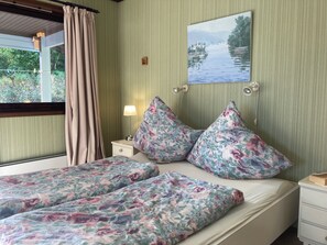 A room with two beds, a window with curtains, a bedside lamp, a wall-mounted picture, and a nightstand with a lamp. - Cozy vacation rental on the Langfjord in Vistdal with panoramic views (Møre og Romsdal)