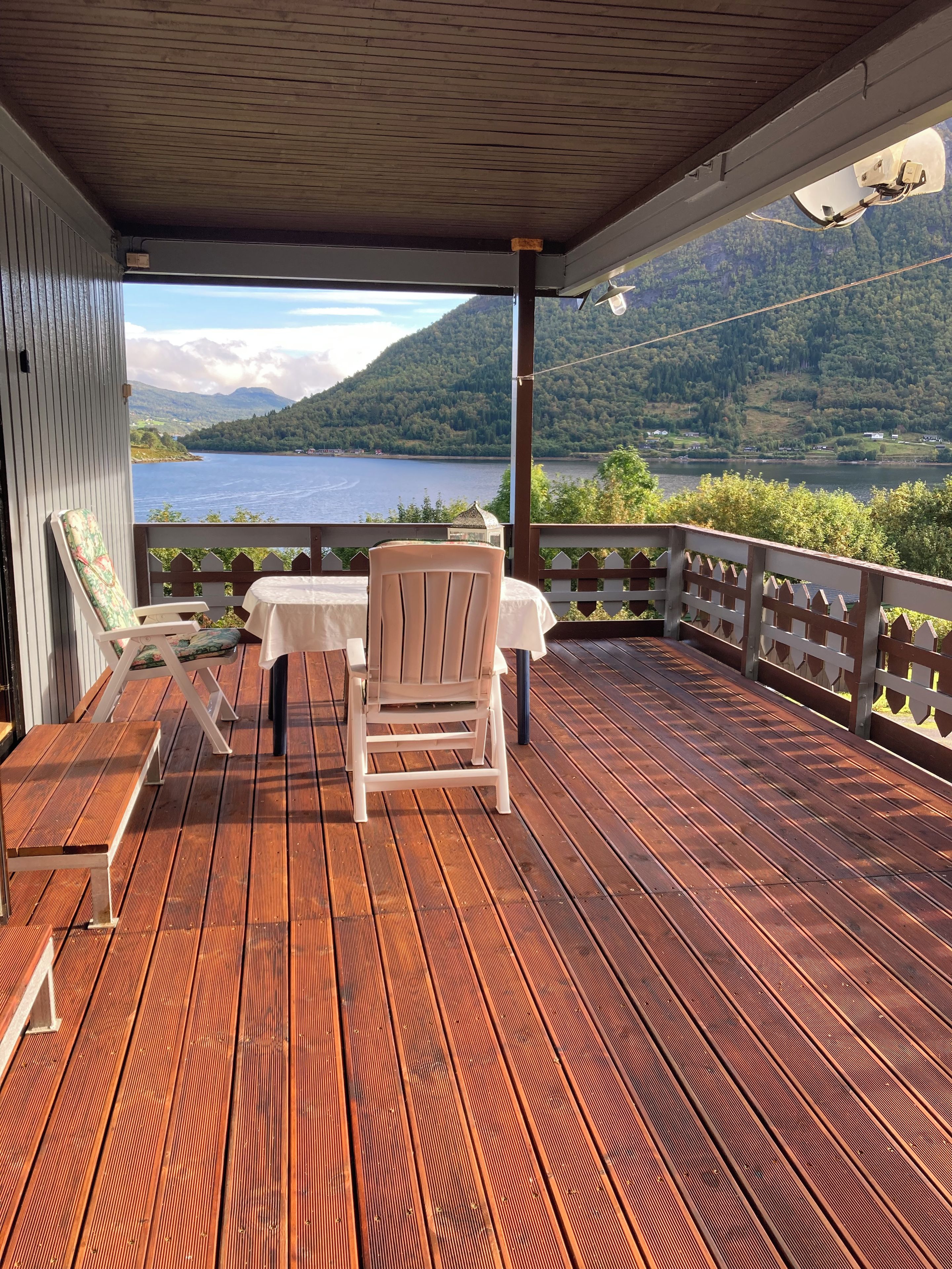 A wooden deck with a table and chairs, overlooking a lake and mountains.