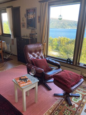 A room with a leather recliner, a small table with a magazine, a window with a view of a lake, and a patterned rug. - Cozy vacation rental on the Langfjord in Vistdal with panoramic views (Møre og Romsdal)