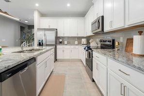 A modern kitchen with white cabinets, stainless steel appliances, and a granite countertop. - Solara 9BR Luxury + Game Room & Pool (Kissimmee)