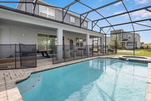 A swimming pool with a glass enclosure, a covered patio area with outdoor furniture, and a view of neighboring houses. - Solara 9BR Luxury + Game Room & Pool (Kissimmee)