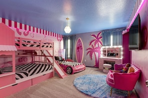 A pink-themed bedroom with bunk beds, a Barbie surfboard, a vanity with lights, and a pink chair. - Solara 9BR Luxury + Game Room & Pool (Kissimmee)