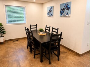 Zona pranzo con tavolo rettangolare, sei sedie, una pianta in vaso e due quadri appesi al muro.