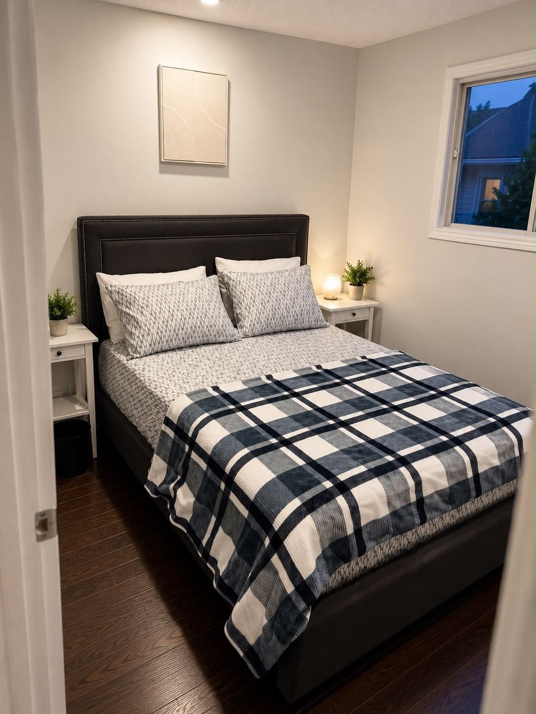 Et soveværelse med seng, sengeborde, en sengetavle, et vindue og en lampe monteret på væggen.