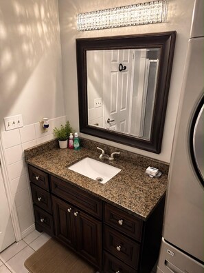 Un bagno con lavabo su piano in granito, mobiletti in legno scuro, un ampio specchio e un frigorifero LG integrato.