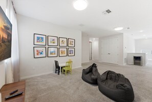 A living room with a carpeted floor, a fireplace, a TV, and framed pictures on the wall. - Solara 9BR Villa w/ Pool, Spa & Game Room (Kissimmee)