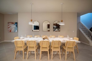 A dining area with a long table, six wicker chairs, and three pendant lights. - 0BR Windsor Cay Home w/ Pool (Clermont)