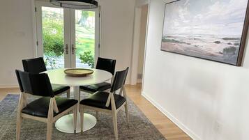 A dining area with a round table, black chairs, a modern pendant light, and a painting on the wall.
