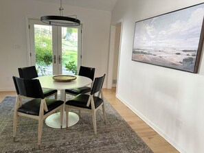 Un comedor con una mesa redonda, sillas negras, una lámpara colgante moderna y un cuadro en la pared.