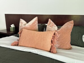 A bed with a dark headboard, multiple pillows, and a tissue box on a nightstand.