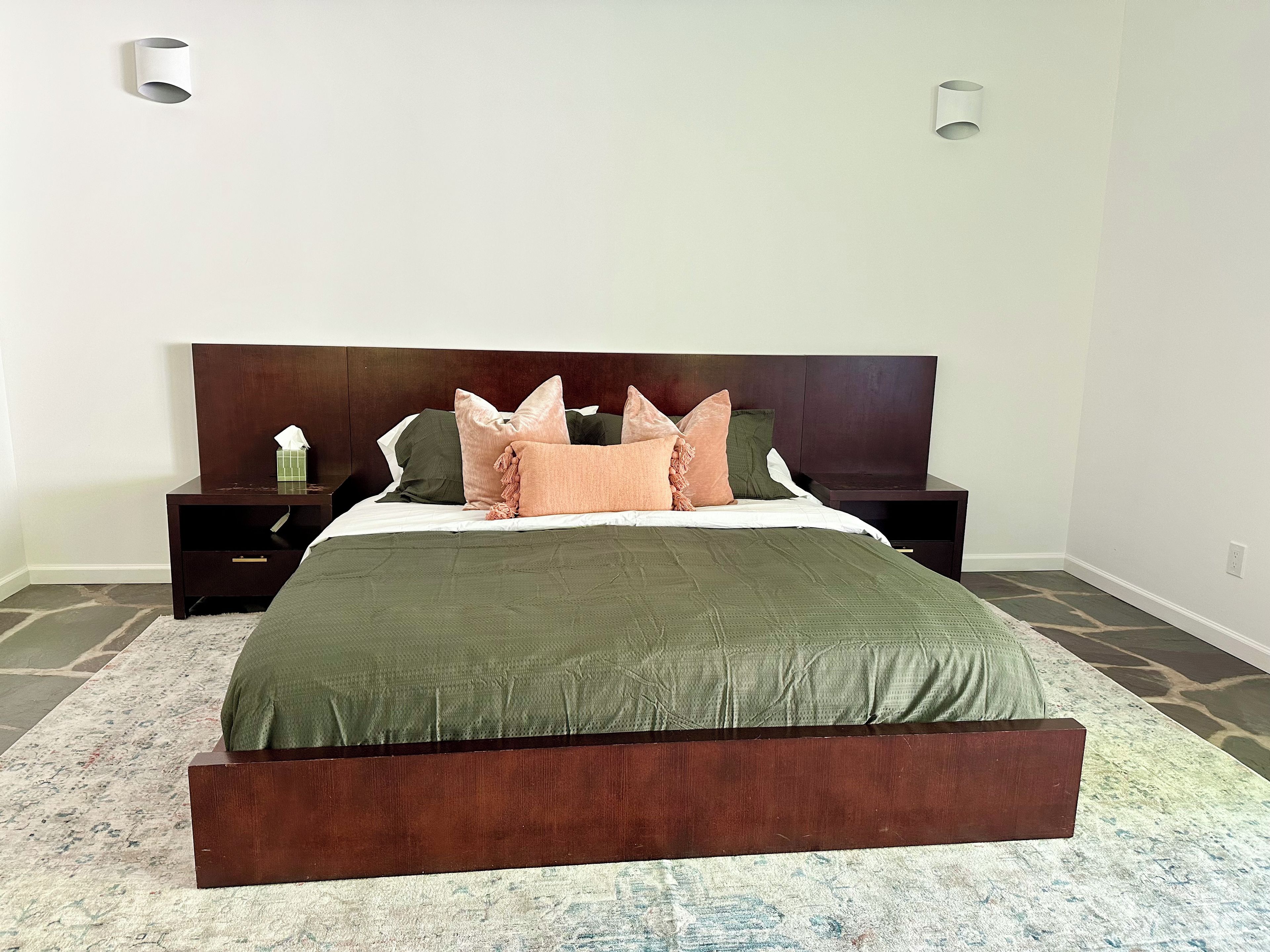 Un dormitorio con una cama grande, cabecera de madera oscura, dos mesitas de noche y un tapete estampado.