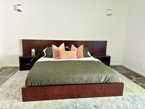 Un dormitorio con una cama grande, cabecera de madera oscura, dos mesitas de noche y un tapete estampado.