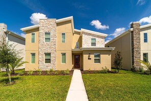 A modern two-story residential building with a stone facade, a red door, and a well-maintained lawn. - Storey Lake 9BR Home w/ Pool & Epic Game Room (Kissimmee)