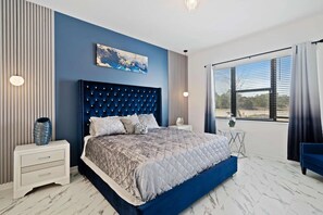Une chambre à coucher moderne avec un grand lit, une tête de lit bleue, un tableau décoratif et une vue par la fenêtre.