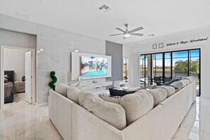A modern living room with a large sectional sofa, a flat-screen TV, and a ceiling fan. - 9-bedroom Mansion in Davenport With Pool and spa (Davenport)