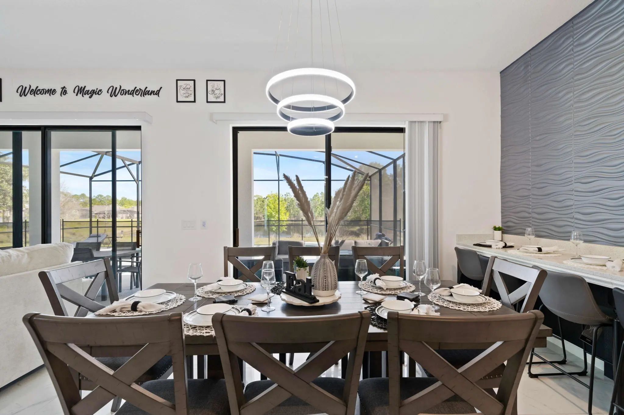 Un espace repas avec une table moderne disposée pour quatre personnes, de grandes fenêtres et une vue sur l’extérieur.