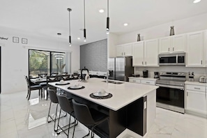 A modern kitchen with white cabinetry, stainless steel appliances, and a large island with bar stools. - 9-bedroom Mansion in Davenport With Pool and spa (Davenport)