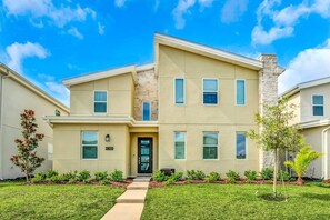 A two-story residential building with a beige facade, a stone chimney, and a front entrance with a door. - Storey Lake 9BR Villa w Pool, Theater, Game Room (Kissimmee)