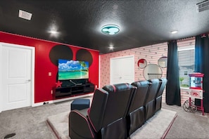 Ein Heimkinozimmer mit einem großen Flachbildfernseher, einer roten Backsteinwand und einer Decke mit Einbautenbeleuchtung.
