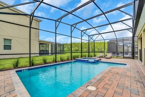 Ein Schwimmbecken mit Glasumrandung, umgeben von einer Ziegelterrasse und einer Rasenfläche.