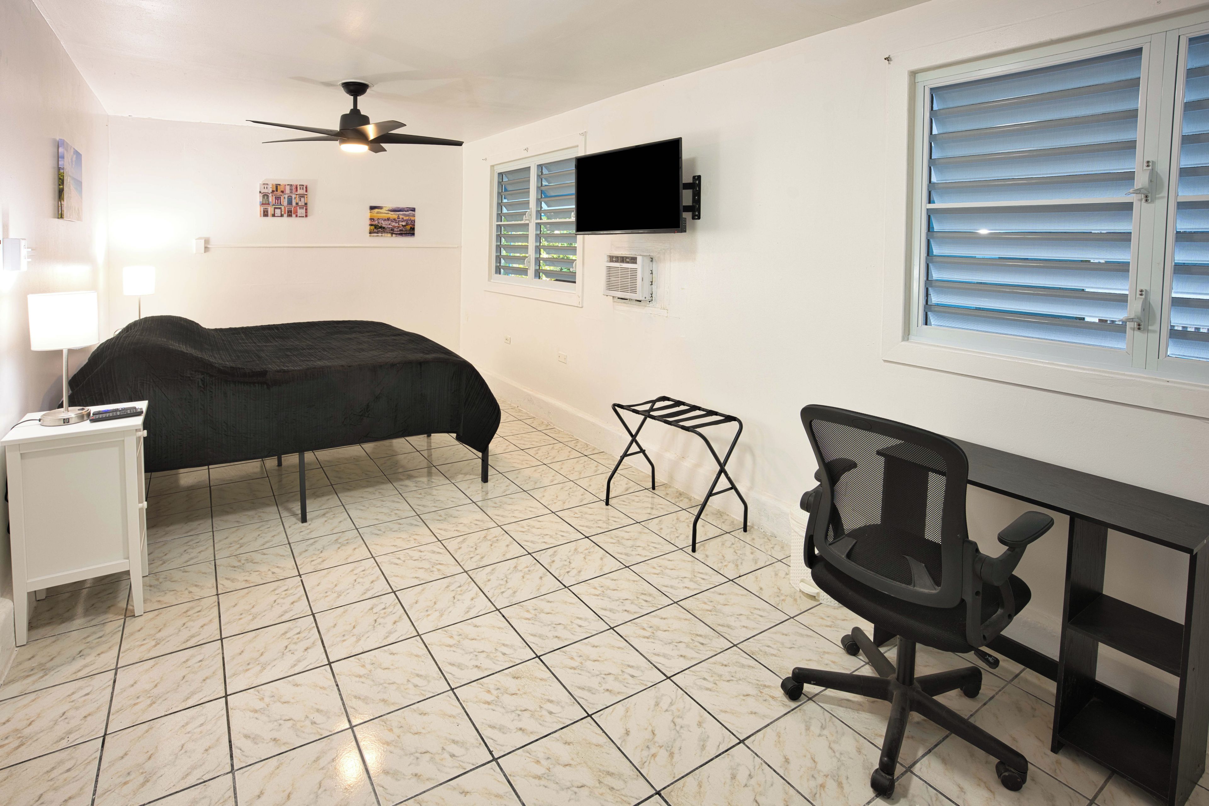 A bedroom with a bed, a desk, a chair, a ceiling fan, and a window with blinds.