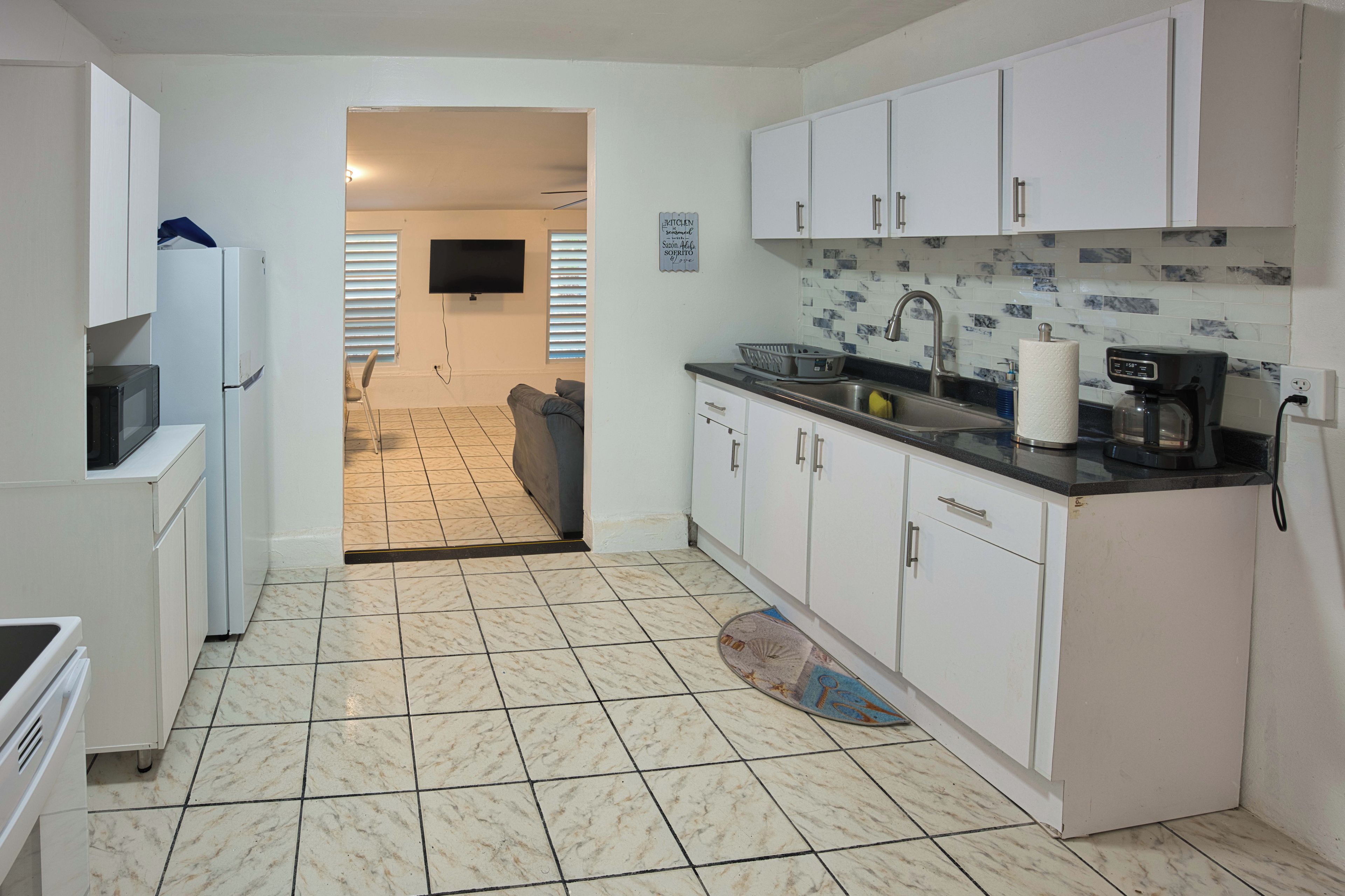A compact kitchen with white cabinets, a tiled floor, a built-in microwave, and a coffee maker.