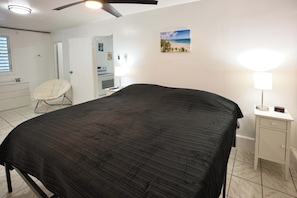A bedroom with a bed, a chair, a desk, a lamp, and a painting on the wall. - Cozy 1-bedroom apartment in serene Aguas Buenas (Aguas Buenas)