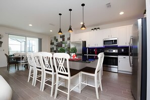 A modern kitchen with white cabinets, stainless steel appliances, and pendant lighting. - 9BR Disney Home w/ Pool, Spa & Theater Room (Kissimmee)