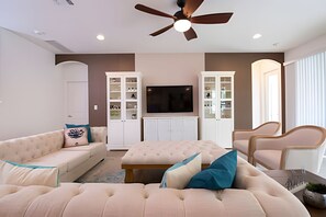 A living room with a sofa, ottoman, and chairs, a television, and built-in cabinets. - 9BR Disney Home w/ Pool, Spa & Theater Room (Kissimmee)