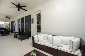 A modern living room with a sofa, ceiling fans, and a dining area with chairs and a table. - 9BR Disney Home w/ Pool, Spa & Theater Room (Kissimmee)