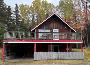 A two-story wooden cabin with a balcony, a covered entrance, and a number sign indicating its location. - Carrabassett Cabin | Minutes to Sugarloaf (Carrabassett Valley)