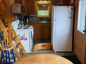 A kitchen with wooden cabinets, a stove, a refrigerator, and a window. - Carrabassett Cabin | Minutes to Sugarloaf (Carrabassett Valley)