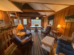 A cozy cabin interior with a dining area, seating, and a staircase. - Carrabassett Cabin | Minutes to Sugarloaf (Carrabassett Valley)