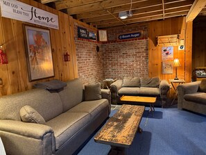 A cozy room with a wooden ceiling, a brick wall, and a couch with a small table. - Carrabassett Cabin | Minutes to Sugarloaf (Carrabassett Valley)