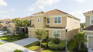 A residential building with a tiled roof, beige exterior walls, and a front yard with a sidewalk and small trees. - 12br Villa w/ Pool Solterra Resort Orlando (Davenport)