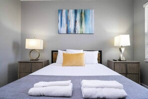 A neatly made bed with white and yellow pillows, two bedside lamps, and a grey blanket. - 12br Villa w/ Pool Solterra Resort Orlando (Davenport)