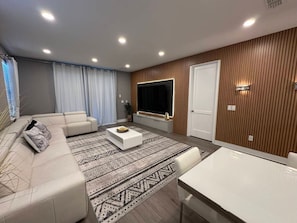 A modern living room with a sectional sofa, a coffee table, a TV, and a dining area. - 9BR Villa w/ Pool & Spa (Kissimmee)