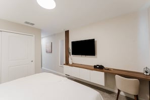 A hotel room with a bed, a TV mounted on the wall, a wooden console table, and a chair. - 9BR Home w/ Pool at Solara Near Disney (Kissimmee)