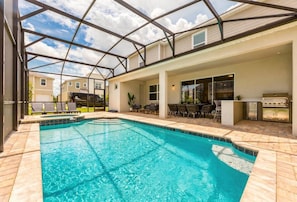 A swimming pool with a covered patio area, outdoor seating, and a grill. - 9BR Home w/ Pool at Solara Near Disney (Kissimmee)