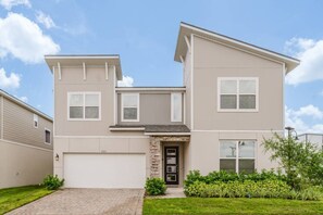 A two-story residential building with a garage, a stone entrance, and a well-maintained lawn. - 9BR Home w/ Pool at Solara Near Disney (Kissimmee)