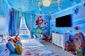 Une chambre à coucher sur le thème du monde sous-marin, avec un lit agrémenté de coussins colorés, une commode et une fresque représentant une scène sous-marine.