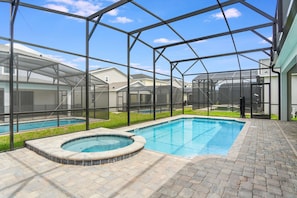 A covered outdoor swimming pool area with a hot tub, surrounded by a metal fence and houses in the background. - Solara Resort 10br Luxury Villa + Private Pool (Kissimmee)