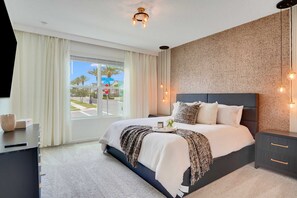 A modern bedroom with a large bed, a bedside table, a nightstand, and a view of the outside. - Solara Resort 10br Luxury Villa + Private Pool (Kissimmee)